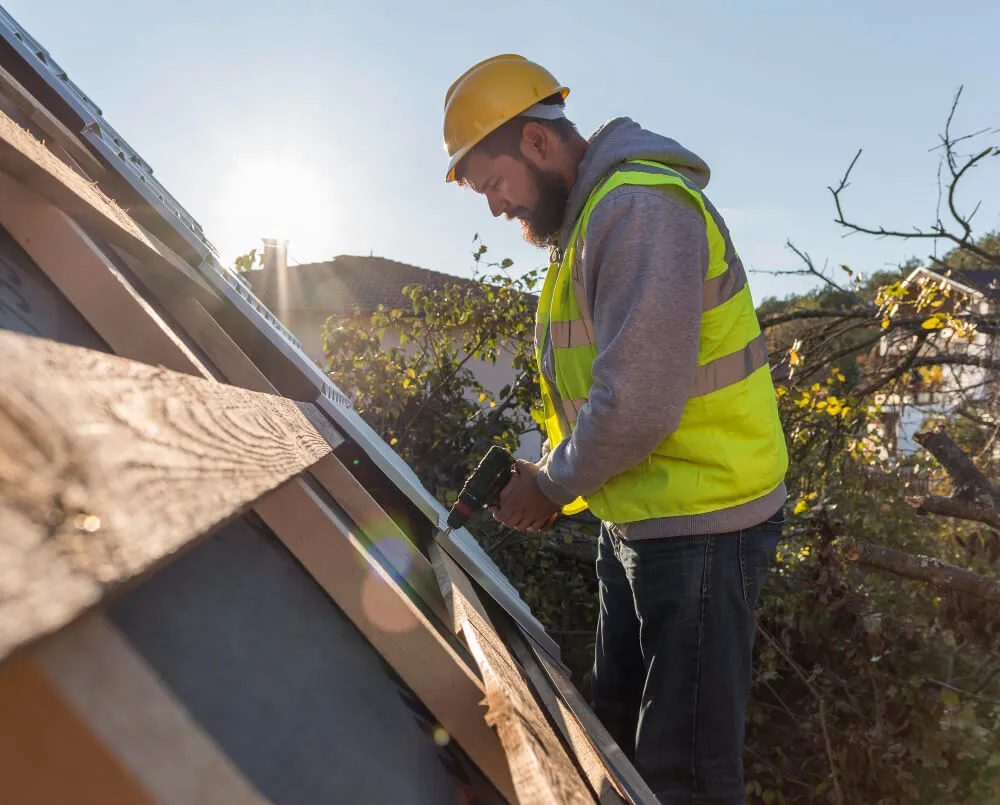 Roofer in yellow vest drilling wood planks on a roof in the sun